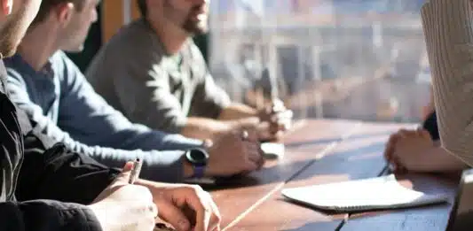 people sitting on chair in front of table while holding pens during daytime